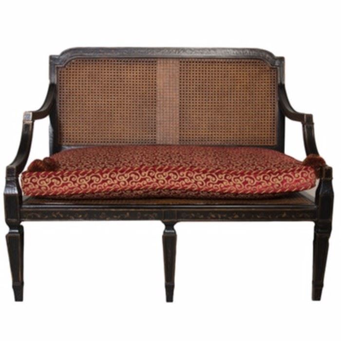 Neoclassical Style Settee by Baker Furniture: A Neoclassical style cane settee by Baker Furniture. The bench features a black lacquered finish with gold tone detailing with vine and leaf accents to the front. It comes with a burgundy and gold tone removable cushion. It is marked “Baker” to the underside.