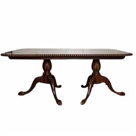 Chippendale Style Double Pedestal Dining Table by Furnitureland: A vintage Chippendale style double pedestal dining table made by Furnitureland. The table has a mahogany stain. There are two pedestals with acanthus leaf accents to the center and on each of the three legs with claw and ball style feet. The table has a dark glass finish and turned border to the top.