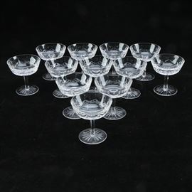 Waterford "Lismore" Crystal Champagne Coupes: A set of twelve crystal champagne coupes in the Lismore pattern by Waterford. Each piece features a shallow, flat-bottomed well with cross-hatched and vertical cuts to the exterior, a hexagonal stem, and a round starburst pattern base. They bear the Waterford watermark on the undersides.