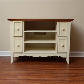 Country Style Television and Electronics Stand: A television and electronics stand. This stand has a stained wooden top and an off-white base with center open shelf storage with two stacked drawers to either side. Located in lower level of home with access to garage.