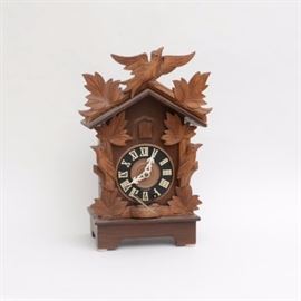 German Made Cuckoo Clock: A cuckoo clock made in West Germany. This fine hand crafted clock is desgined with a bird in flight to top with leaves to either side which follows down the sides. A black face with white Roman numeral hour markers and pierced hands. A little bird will appear from behind closed door. Key is present.