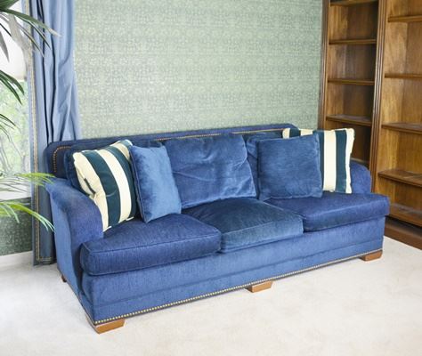 Stanford Furniture Navy Upholstered Sofa: A Stanford Furniture navy upholstered sofa. Upholstered in a chenille-velour type fabric with matching welting, this three seat sofa features removable back and seat cushions, a square back design, brass nailhead trim and wood feet. The back cushions include a blend of 50% feathers/50% synthetic fibers. The seat cushions include a blend of 20% feathers/80% synthetic fibers. There are also two matching square feather pillows with zippered covers and two square striped accent pillows.