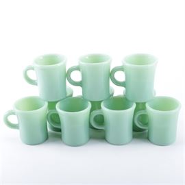 Fire-King Jadeite Mugs: A set of ten Fire-King Jadeite glass mugs. Each piece is presented in the iconic jade green color. They are marked to the underside, “Fire-King, Oven Ware”.
