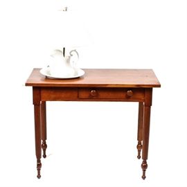 Wooden Washstand and Lamp: An antique hardwood washstand. This table features a rectangular top with a circular cut-out for the included ewer in bowl ceramic lamp. The table has a singular, shallow drawer with dual round knobs and rests upon carved feet. The washstand and ewer are unmarked by maker.