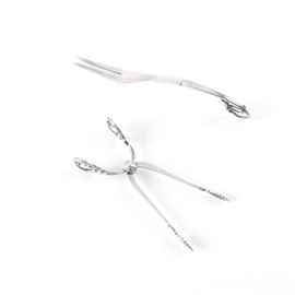 Georg Jensen "Ornamental" Sterling Fork and "Blossom" Sugar Tongs: A pairing of sterling silver flatware by Danish silversmith Georg Jensen. This includes a two-tine cold cut serving fork in the Ornamental #21 pattern, featuring a curved, Art Nouveau style handle with beaded and flower petal tip. It is stamped to the back “21 Denmark Sterling” alongside the “GI” beaded maker’s mark, dating this piece to circa 1910-1925. Also presented are a pair of sugar tongs in the Blossom pattern with leaf-shaped tips and flower bud designed handles. It is marked to one side “Sterling” and to the other “Denmark”. The total approximate weight is 1.335 ozt.