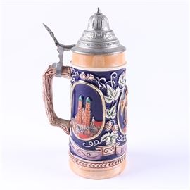 Ceramic Beer Stein: A ceramic beer stein. This lidded beer stein is decorated with images of buildings in Munich, Germany flanking a man holding two beer steins above the word “München”. The stein is marked “Gerz Made in Germany” to the underside.