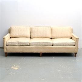 Vintage Mid-Century Sofa: A vintage mid-century sofa. It has three removable back and seat cushions, straight armrests, and a straight front, raised on tapered block legs. It is upholstered throughout in a cream colored fabric with lattice design.