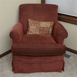 Upholstered Swivel Glider: An upholstered swivel glider. The chair has a wood frame and features a burnt red corduroy upholstery with cloth piping. Other features include a club style with a square back, rolled arms and a loose cushioned seat and a pleated skirt.