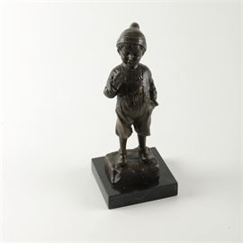 Metal Sculpture of Boy: A metal sculpture of a boy. This bronze tone sculpture depicts a boy adorned in a cap and overalls mischievously posed with his hand in one pocket, looking down at what appears to be a cigarette in his mouth. He stands on a chiseled rock which is affixed to a polished, black marbleized base with a felt underside for support.