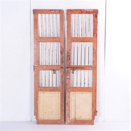 Pair of Rustic Doors: A pair of rustic doors. Each door features a framed row of metal spindles with support rails dividing vertical into sections with a panel underneath. The doors include decorative slide-bolt hardware and hinges and they have a heavily distressed finish including orange and yellow hues.