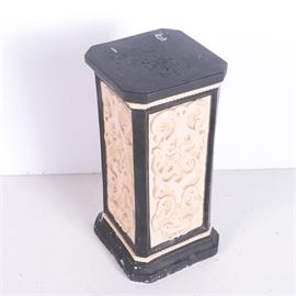 Ceramic Display Pillar: A ceramic pillar display stand. The stand features a square top with chamfered corners, rope molding, and a scroll pattern in relief on the side panels. The stand is painted black with cream tone panels and rope trim. the base repeats the angled corners of the top.