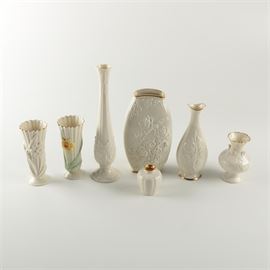 Collection of Lenox Porcelain Vases: A collection of porcelain vases by Lenox. This group includes seven vases with white glazed surfaces and embossed flowers, as well as a few with gilt trim. It features two with scalloped lip and daffodils, a tall thin vase from the Florentine Collection, one from the Sharon Collection, one from the Elfin Collection, and more. The undersides are all marked with the Lenox maker’s mark.