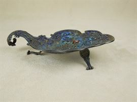CW:  Antique plique-à-jour silver footed miniature dish with scroll handle.  Enameled with a central peacock, birds and butterflies.  Unmarked.  Circa 1900.  5" x 3.2" x 1" high
