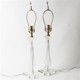 Pair of Crystal Table Lamps: A pair of crystal table lamps. This features two matching vintage table lamps each with a harp and crystal finial and one light socket and a pillar style crystal body with a Corinthian capital on a square base.