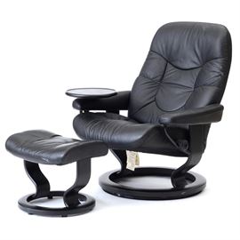 Black Leather "Stressless" Adjustable Chair and Ottoman by Ekornes / Norway: A black leather upholstered “Stressless” lounge chair with adjustment knob and ottoman, by Ekornes of Norway. The chair and ottoman have laminated wooden frames, stained black and each having a circular base.