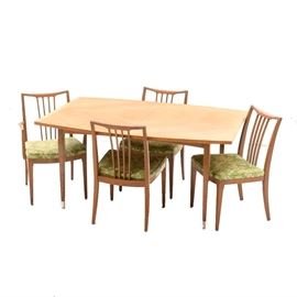 Mid Century Modern Dining Set: A Mid Century Modern dining set with chairs. The table features a veneer book matched top in a blond wood with banding to the edge. Included with the table are pads and two extensions. The table extensions do not match the table but fit. Comes with four chairs that display slat back splats with a gently curved crest over a fixed upholstered seat comprised from a green and cream floral fabric.