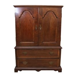 Wardrobe by Century: A contemporary wardrobe by Century Furniture. It has a beveled cornice over a pair of flame mahogany arch paneled doors with brass drop pulls on pierced plates. Inside the cabinet is a long shelf, divided shelf, and long drawer. The cabinet sits on a pair of long, stacked drawers with border to the face, and brass bails on pierced batwing plates. The piece stands on corner bracket feet. It’s maker’s mark is inside a drawer.