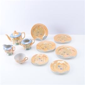 Small Japanese Porcelain Tea Set: A Japanese small porcelain tea set. The set includes a covered teapot, a double handled sugar bowl, a creamer, a tea cup, three saucers and three small plates. The set have an opalescent peach glaze with an outdoor mountainous scene featuring flowers, flying birds and clouds on one side of the rims of the plates. The set is marked “Made in Japan” on the bases.