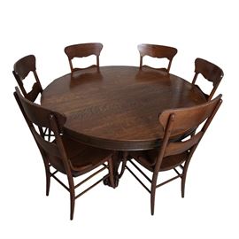 Dark Stained Oak Dining Table with Six Chairs: An oak pedestal table and six chairs. The dark stained table has a circular top on center pedestal, which ends on paw feet. It separates in the center to fit three extension leaves. The dark stained oak chairs have a wide top rail, scalloped to the underside, over a serpentine curved cross rail. They have curved hip supports on either side of the scooped seats, and tapered legs that connect with double box stretchers and splay out at the feet.