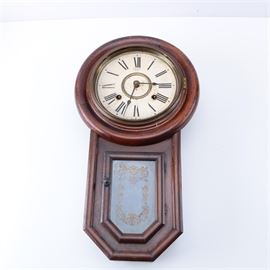 Japanese Vintage Sato's Wall Clock: A Japanese vintage Sato’s wall clock. The clock is a regulator style with a rectangular shaped mahogany case that features a round wood frame surrounding a hinged brass bezel and glass cover door that displays a white face with black Roman numerals and hands. Other features of the clock include a long drop with beveled edges and a brass hinged glass front door with a gilded foliate design. The clock has a brass pendulum, chimes, a hook to the verso for hanging and is labeled “Sato’s Clock Factory”. to the interior. The clock was made in Japan for export by The Sato’s Clock Factory, circa 1925.