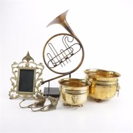 Assorted Brass Décor: An assortment of brass décor. This assortment consists of six items. Included in this assortment are two brass horse head hook hangers, a picture frame, two planters accented with lion head side handles and footed bases, and decorative trumpet. The items are surfaced in variations of a brass and gold tone finish.