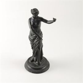 Cast Iron Sculpture of Grecian Style Woman: A cast iron sculpture of a Grecian style woman. This sculpture depicts a semi-nude woman standing with a slight bent knee, tilting her head downward while lifting one arm in the air. Her torso is draped with cloth, and she wears an ornate crown. The figure is fitted on a turned base that is unmarked.