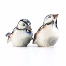 Pair of Goebel Bird Figurines: A pair of Goebel bird figurines. This pair features two bird figurines depicting one seated bird looking up while another seated bird is looking down. The figurines are glazed in colors of white, black, orange, brown, and blue with a glossy finish. The undersides of the figurines are marked, “Goebel W. Germany.”