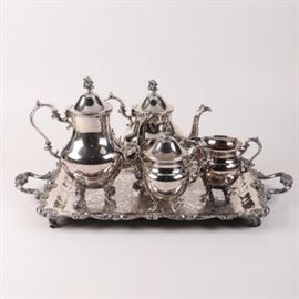 English Silver Mfg. Corp Silver on Copper Tea Service: A silver on copper tea service by English Silver Mfg. Corp, founded in the 1950s out of Brooklyn, NY. The set includes a coffee pot, a teapot, a lidded creamer, and a sugar. The items feature fluted forms with ornately scrolled handles atop four scrolled feet. The lids are adorned with branch and berry finials. Items are marked “English Silver Mfg Corp, Made in USA, Silver on Copper” with “TR” in a circle, “MRRS” in a cartouche, and a man’s profile. Items present on a rectangular tray with an engraved center, double handles, and a scrolled rim.