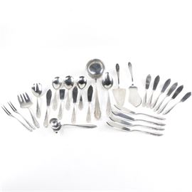 800 Silver Flatware Set: A twenty-six piece 800 silver flatware set. The set features beveled edges on the handles with an elongated scalloped design. Each piece has a personalized engravings on the handles. Included in the set is a serving spoon, a pie server, an ice cream server, a serving fork, a soup ladle, a gravy ladle, a blunt tipped server, a salad serving fork, three spoons, two two-pronged berry forks, a 7.75 inch butter knife, and twelve fish knives. The pieces are marked with a crescent moon, a crown, “800” and a makers mark. All together the pieces weigh approximately 58.50 ozt.