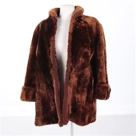 Women's Sheared Beaver Fur Coat: A women’s sheared beaver fur coat. The brown fur coat features a flip collar with a button closure at the throat, a prong and loop fastening at the waist, seam pockets and cuffed sleeves. The coat includes a fully lined interior.