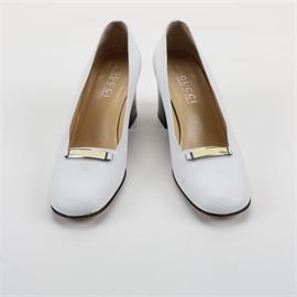 Women's Gucci Leather Pumps: A pair of women’s Gucci leather pumps. The slip on shoes, size 7 B, feature white leather uppers, round toes, a metal and enamel logo bar on the vamp and stacked block heels. The shoes include brand stamps on the insoles and soles, and are stamped on the lining, “101 2310”.