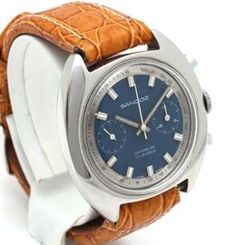 Sandoz Stainless Steel Wristwatch: A Sandoz stainless steel wristwatch. This wristwatch features a padded stitch leather band secured to a round case. The dial background is blue with hour index markers extending out into view. Two sub dials are positioned on either side of luminous styled hands.