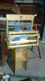 small loom, glass case is located behind the loom 