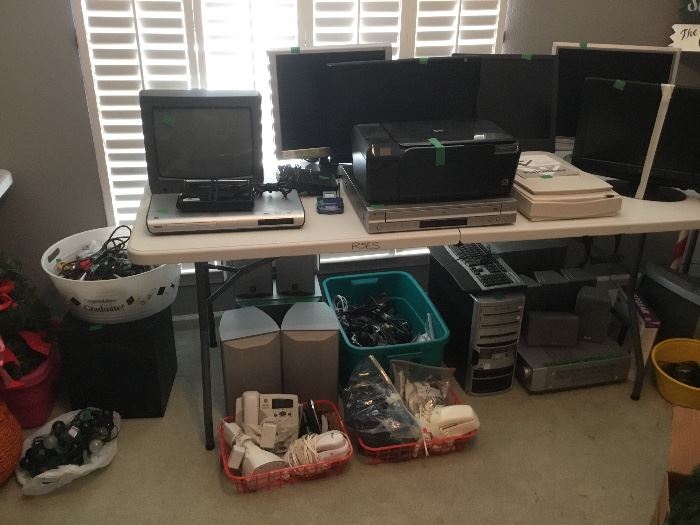 Table full of monitors, speaker sets,  scanner, DVD players,  phones & electronics 