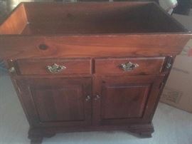 Antique wooden dry sink with brass fixtures. The top flap folds down. Two drawers and shelf inside cabinet.