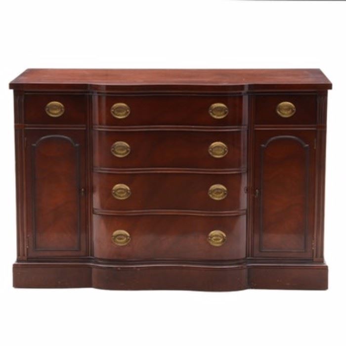 "New Hampton Court" Sideboard by Drexel: A Drexel sideboard from the “New Hampton Court” collection. This piece is designed with a serpent front, mahogany veneer, reeded side rails and finished with stamped sheet-brass backplates with bail handles. It has six dovetail jointed drawers and two side cabinets. It is stamped to the interior “By Drexel Registered Trademark.” The back is marked with “430 I-3P New Hampton Court 3-9-55.”