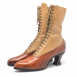 Women's Victorian Boots: A pair of women’s Victorian boots. These lace-up boots feature two-tone leather construction, seventeen eye lace-ups, a 2 1/4" stacked heel and leather tongue. The natural brown lower is complimented by the mustard colored leather of the upper part of the shoe and the stacked heel features a decorative metal band.