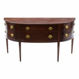 Federal Style Mahogany Stained Demilune Buffet: A Federal style mahogany stained demilune buffet. This wood buffet features six drawers, with brass tone oval pulls and dovetail construction. It also includes two sets of faux drawers on each end, with a flat surface edge, flush drawer fronts, and tapered legs. The top center drawer includes a divided compartment for utensils.