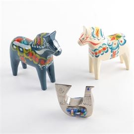 Nils Olsson Swedish Painted Wooden Horses: A pair of Nils Olsson Swedish painted horses. The horses are carved of wood, one is painted blue and one white. Each horse features a colorful design. The blue horse is signed “Prester” to the rear and both horses are marked with a “Nils Olsson” label to the underside. Also included is a silver plate bird etched with a geometric design and inlaid with jewels.