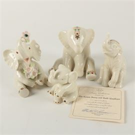 Set of Four Lenox Fine China Elephants: A collection of Lenox fine china elephants. The collection features four elephants in ivory fine china accented with gold details. The largest elephant is accompanied by a certificate from Lenox and signed by Martha A. Curren, President of Lenox. All of the elephants are marked to the bottom in gold with Lenox.