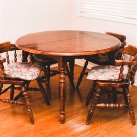 Vintage Wooden Dining Table with Captains Chairs: A wooden dining set with a table and four chairs. Each Windsor chair has banded spindles and legs with H stretchers. The table, which is expandable, has two additional leaves that expand the circular table into an oval. Seat cushions included.