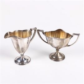 Antique Weighted W.H. Saart Co. Sterling Silver Creamer and Sugar Bowl: An early 20th Century weighted sterling silver creamer and sugar bowl set by W.H. Saart Co. The items feature elongated forms with wavy rims, angular handles, and round footed bases. The undersides are marked “Weighted Sterling” with the W.H. Saart Co. maker’s mark.