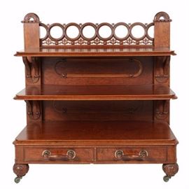 Antique Victorian Three-Tier Walnut Server: An antique Victorian three-tier walnut server, circa third quarter of the 19th century. The frame features a rear gallery with a row of openwork rings supported by pierced foliate motifs alternating with cabochons. Flanking the gallery is a pair of square posts topped by arches with shallow-carved leaves and berries against a stippled ground. Directly below are three rectangular shelves with figured veneers, molded edges, and rounded corners supported by leaf- and berry-carved brackets. The two lower, back panels are applied with racetrack moldings and the base is fitted with two aligned, dovetailed drawers. The fronts have spindled handles with ball terminals and the server rises on ball-carved, front feet ending in brass casters.