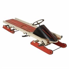 Vintage Toboggan Sled with Steering Wheel: A vintage toboggan sled with a steering wheel. The wooden, white- and orange-painted frame features a pointed, black metal nose backed by a steering wheel above a slatted platform. The side rails are applied with six metal handles and the sled rises on two pairs of shaped runners. Orange and black pinstripes decorate the nose and platform and there is a rope attached to the front. It is unmarked.