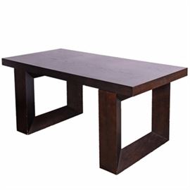 Modern Style Large Wooden Desk: A Modern style dark wooden laminated and wooden large desk/ table. This piece has a rectangular top with a single drawer to one side, flush with the plain apron. It is raised on two open square legs, with inward angles accenting the blocks. The top can be removed from the legs.