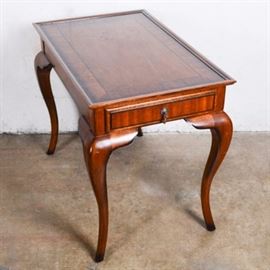 Continental Style Mahogany End Table: A Continental style mahogany end table. This rectangular table features a veneered walnut top with cross banded borders and pin line details and includes a tray style edge. One raised panel drawer with a black border and teardrop pull is tucked into the apron. It stands on cabriole legs with French flared feet.