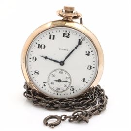 Open Face Elgin Pocket Watch: A 1926 Elgin open face pocket watch. This timepiece features a white enamel face, with Arabic and slash numerals, a sunk seconds sub-dial at the 6 o’clock position. The case is gold filled and monogrammed R.L.S.; with a vintage base metal fob attached.