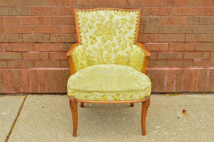 Louis XVI Style Armchair: A Louis XVI style armchair. This floral upholstered chair features a serpentine shaped crest rail over an upholstered back and seat flanked by scroll arms. The seat rises above saber legs with carvings to the knees.