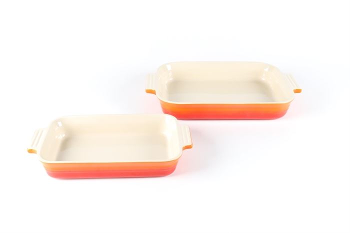 Le Creuset "Flame" Cast Enamel Bakeware: A set of two Le Creuset baking dishes with handles. Both rectangular baking pans are made from cast iron enameled in the red and orange Flame color. The bakeware is marked to the underside “Le Creuset”.