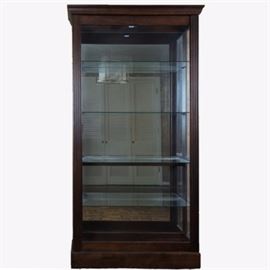Pulaski Furniture Illuminated Display Cabinet: An illuminated glass display cabinet by Pulaski Furniture. This large lighted vitrine features a sliding door front, four adjustable glass shelves, halogen lighting, and a mirrored back panel. The frame is constructed of solids and veneers with a walnut finish. All glass is clear. This item is located on the main level of the home. Professional movers are suggested.